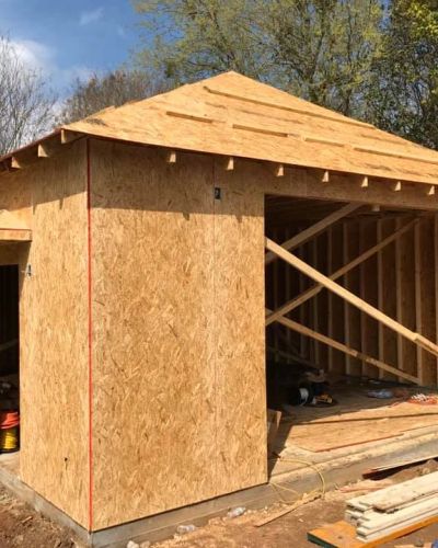 Detached garage under new construction with OSB sheathing on walls and roof, surrounded by tools and building materials.